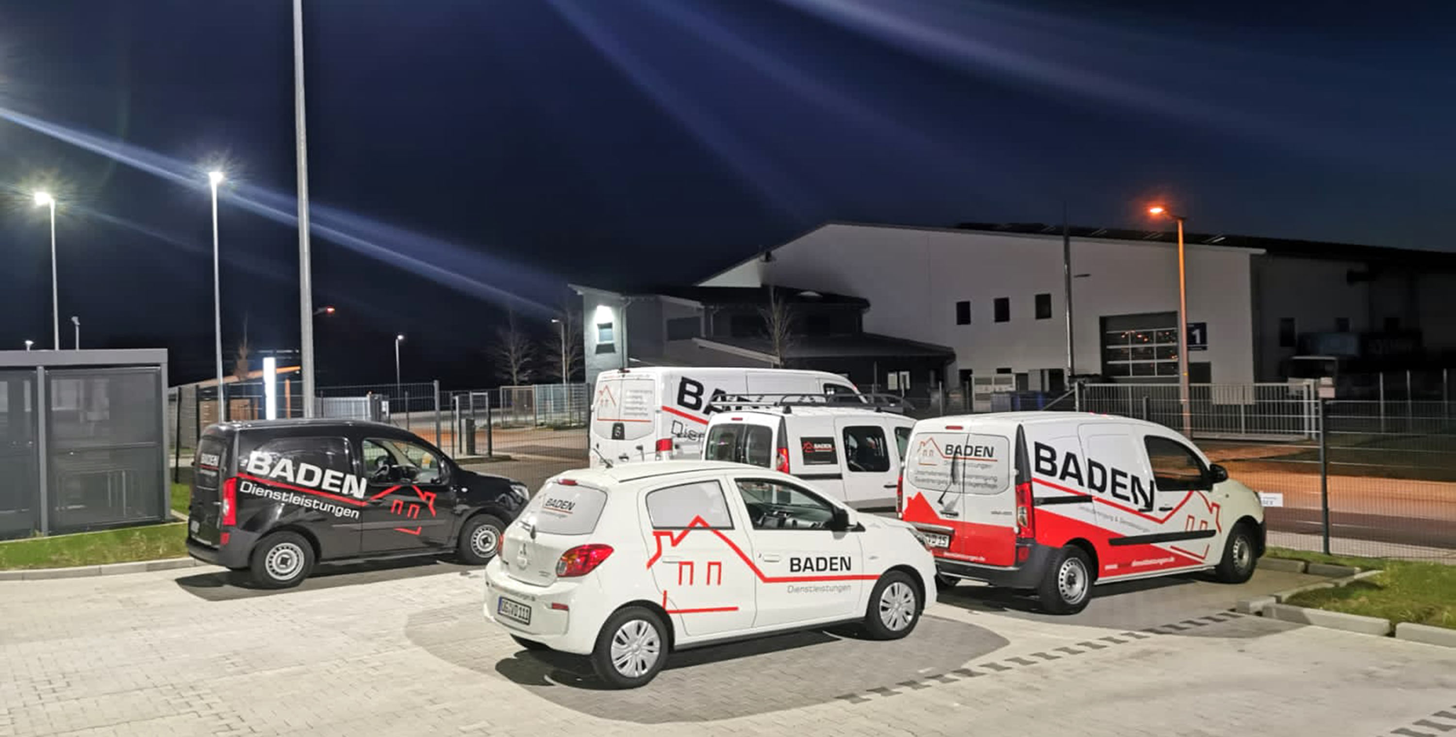 Beleuchtete Firmenfahrzeuge von Baden Dienstleistungen aus Offenburg auf einem Parkplatz bei Nacht